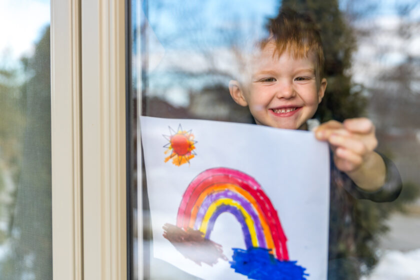 little boy holding up his painting to show it off.